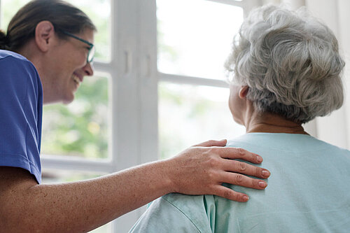 Caring Woman in scrubs with hand on shoulder of older woman